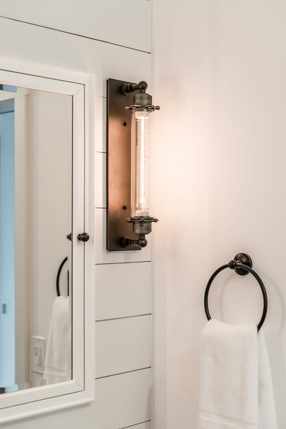 Bronze antique light fixture on shiplap wall near metal towel ring and medicine cabinet mirror after renovation